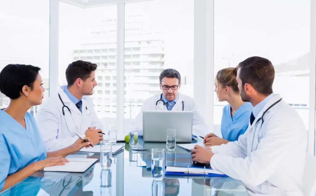 Doctors collaborating around a table in a bright medical coworking space with city views.