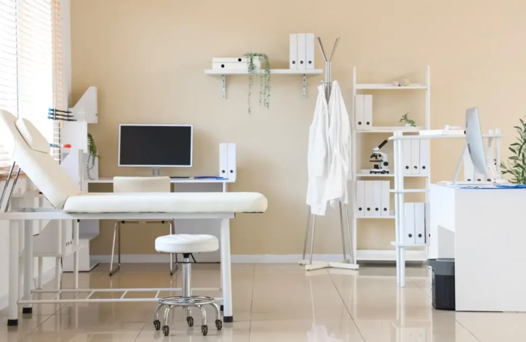 Modern and clean medical office space with an examination bed, desk setup, and organized shelving in a professional clinical environment.