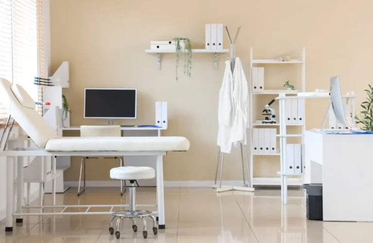 Modern and clean medical office space with an examination bed, desk setup, and organized shelving in a professional clinical environment.