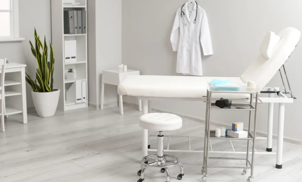 Minimalist medical office space featuring a white examination bed, medical stool, supply cart, and clean modern decor